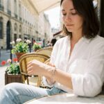 Jeune femme portant un bracelet ancre en argent au poignet dans un café parisien, style casual chic